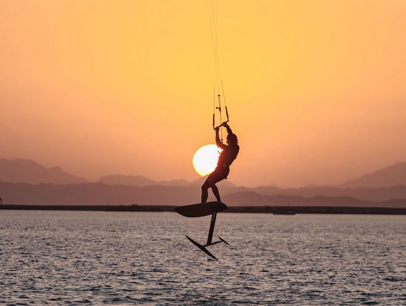 Kite foiler jumping against the setting sun, with the mast and wings visible under the board