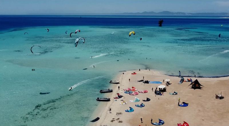 A kite camp on a white sandbank and dozens of kites on the water