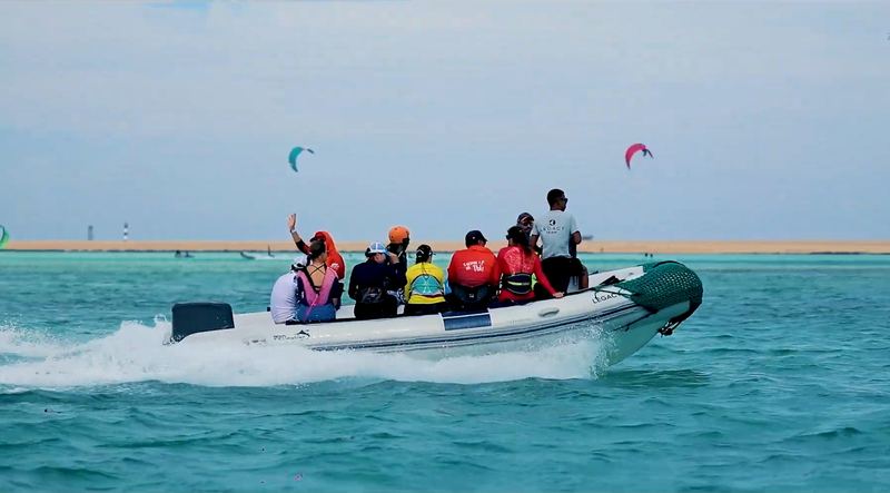 A RIB full of smiling kiters heading out, kites over the lagoon