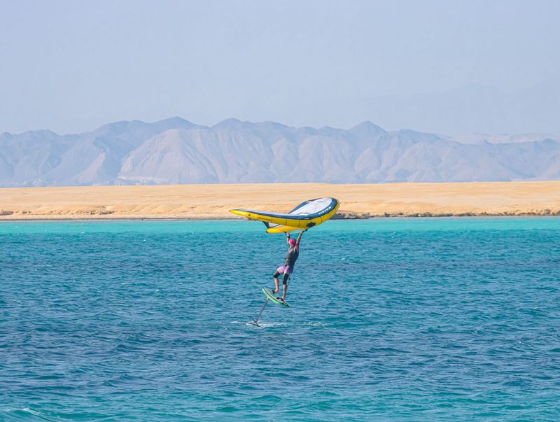 Wing foiler gliding in front of an island and desert mountains