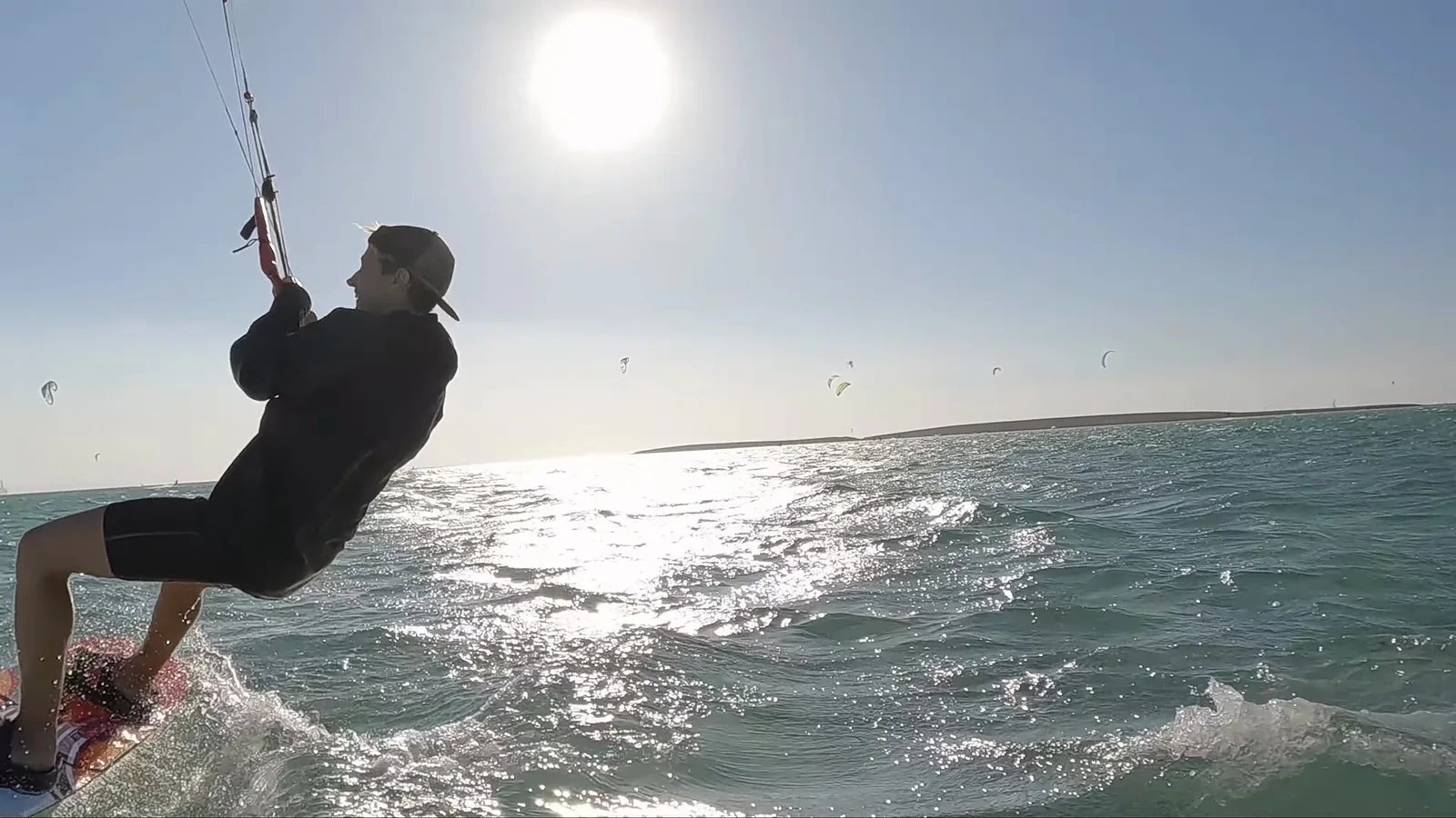 A backlit kiter right by the camera, the sun and more kites behind